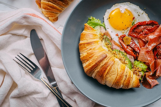Köstliches Croissant-Frühstück gefüllt mit Ricotta und Avocado mit sonnengetrockneten Tomatenstückchen Jamon-Spiegelei