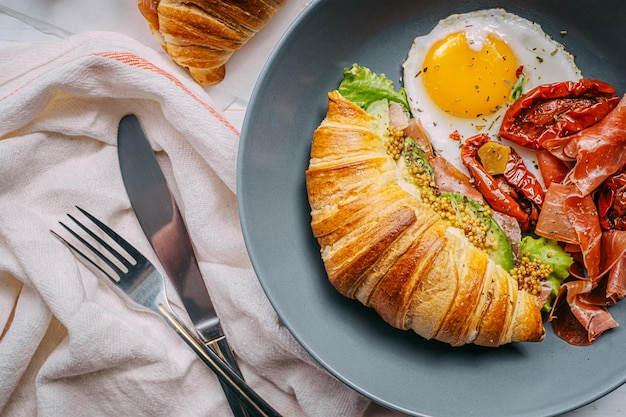 Köstliches Croissant-Frühstück gefüllt mit Ricotta und Avocado mit sonnengetrockneten Tomatenstückchen Jamon-Spiegelei