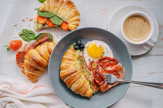 Köstliches Croissant-Frühstück gefüllt mit Ricotta und Avocado mit sonnengetrockneten Tomatenstückchen Jamon-Spiegelei