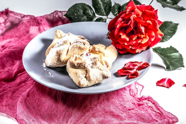 Köstliches frisches romantisches Frühstück mit Keksen und einer Rose auf einem rosa Tuch, süß, Dessert.