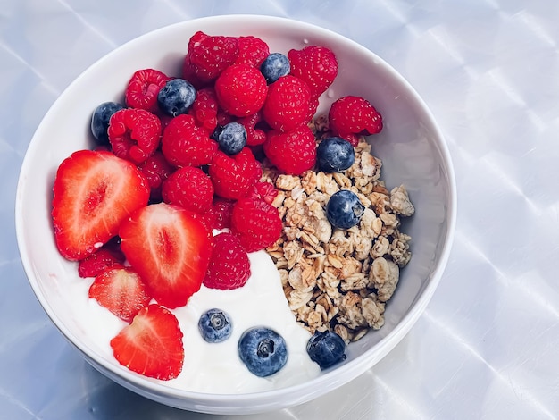 Köstliches Frühstück mit Müslijoghurt, Erdbeeren, Himbeeren und Heidelbeeren im Garten im Freien, gesunde Ernährung und Ernährung