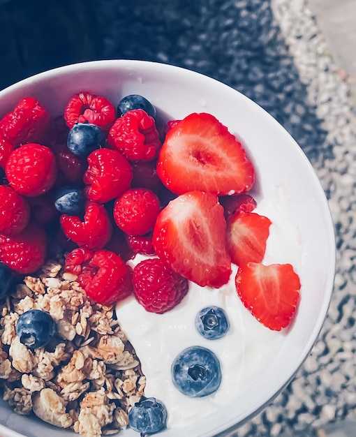 Köstliches Frühstück mit Müslijoghurt, Erdbeeren, Himbeeren und Heidelbeeren im Garten im Freien, gesunde Ernährung und Ernährung