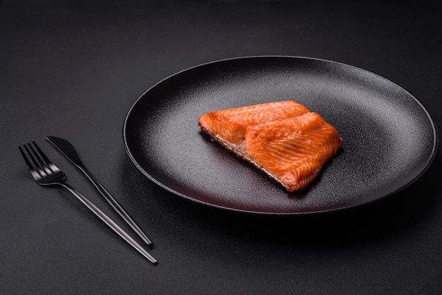 Köstliches gebackenes lachsrotes Fischsteak mit Gewürzen und Kräutern auf dunklem Betonhintergrund