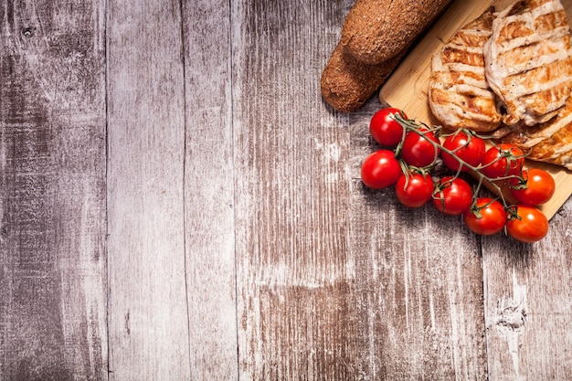 Köstliches gegrilltes Hähnchen auf Holzbrett neben gesundem Brot, Tomaten und Salat. Gesunder Lebensstil und gesunde Ernährung