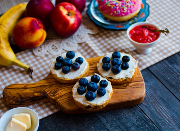 Köstliches gesundes Frühstück, Fruchtsandwiche mit verschiedenen Füllungen, Käse, Banane, Erdbeere, Fischen, Butter, Blaubeere, auf einer anderen Holzoberfläche.