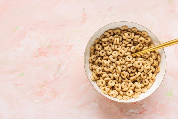 Köstliches Honig-Cheerios-Müsli in einer Schüssel und einem goldenen Löffel auf rosa Hintergrund Draufsicht-Kopienraum