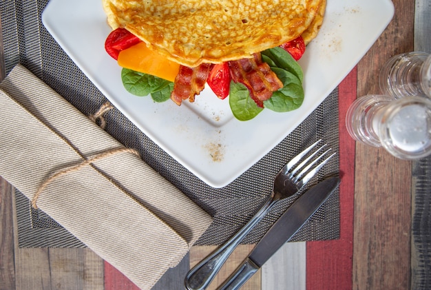 Köstliches nahes hohes Omelett mit Käse, Grilltomate Schinken, knusperigem Becon und Salat