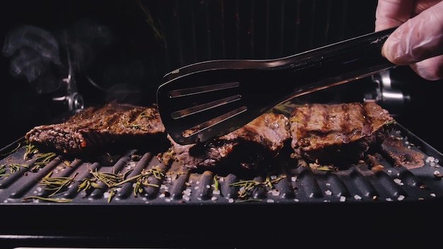 Köstliches saftiges Fleischsteak, das auf dem Grill kocht. Küchenzange