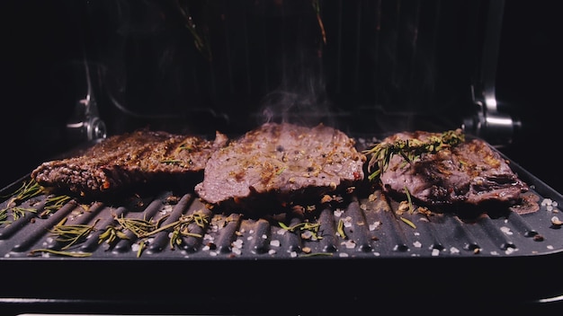 Köstliches saftiges Fleischsteak, das auf dem Grill zubereitet wird Prime Beef Fry auf Elektroröster Rosmarin schwarzer Pfeffer Salz Zeitlupe