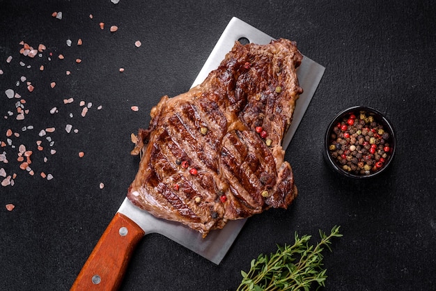 Köstliches saftiges frisches Rindersteak mit Gewürzen und Kräutern auf dunklem Betonhintergrund. Grillgerichte