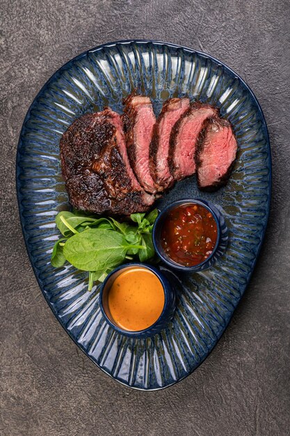 Köstliches saftiges gegrilltes Stück gegrilltes Steak mit Spinat und Saucen auf einem glänzenden blauen Teller Geschnittenes Steak Medium rare Ein herzhaftes Gourmet-Mittagessen Restaurantversorgung