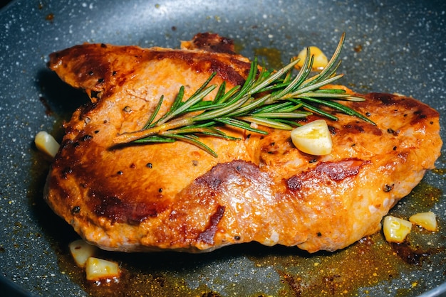 Köstliches saftiges Schweinesteak gewürzt mit Rosmarin und Knoblauch wird in einer Pfanne gebraten.