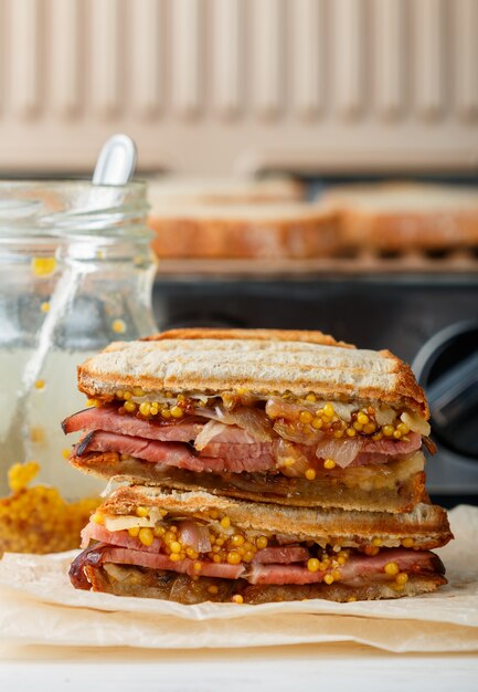 Köstliches Sandwich mit Fleisch, gebratenen Zwiebeln, Käse und Senf auf dem Grill, Abendessen der Männer