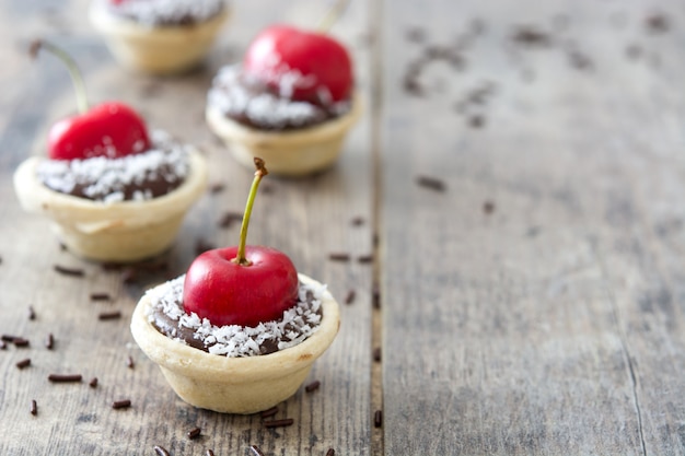 Foto köstliches schokoladentörtchen mit kirsche und kokosnuss auf holztisch