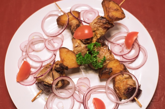 Köstliches Schweinefleisch und Gemüse, das auf Holzstäbchen geschnitten wird, mischen gegrilltes Fleisch auf einem weißen Teller