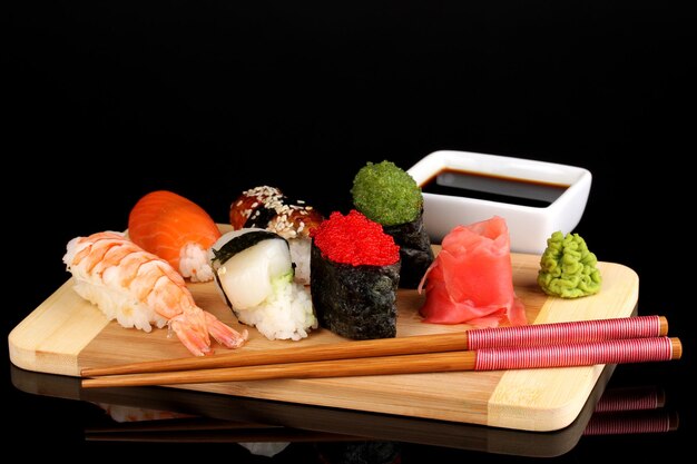 Köstliches Sushi serviert auf Holzbrett isoliert auf schwarz