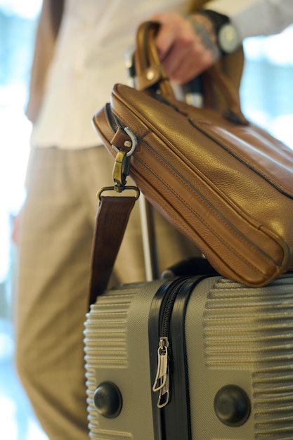Koffer mit Gepäck und brauner Lederhandtasche, die von jungen männlichen Reisenden gehalten werden