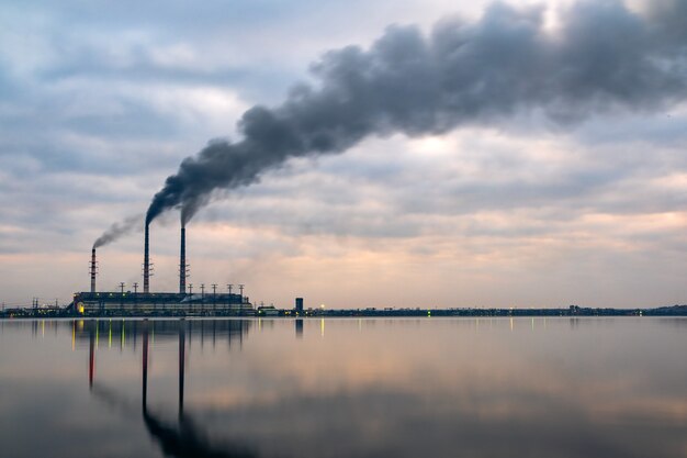 Kohlekraftwerk hohe Rohre mit schwarzem Rauch, der sich nach oben bewegt, verschmutzende Atmosphäre mit Reflexionen