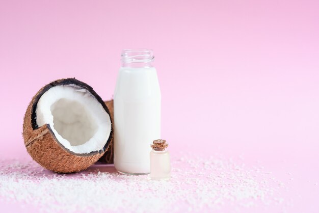 Kokosmilch in der Glasflasche, Kokosflocken, Öl und frische Kokosnuss auf rosa Hintergrund.