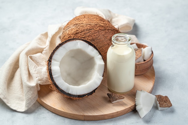Kokosmilch in einer Flasche und Kokos auf grauem Hintergrund. Kuhmilchersatz. Gesundes, natürliches Getränk.