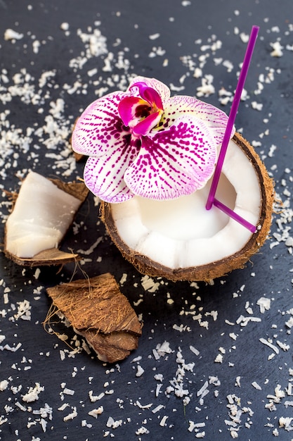 Kokosnüsse mit Kokosnussflocken und -orchidee auf dem grauen Stein backg