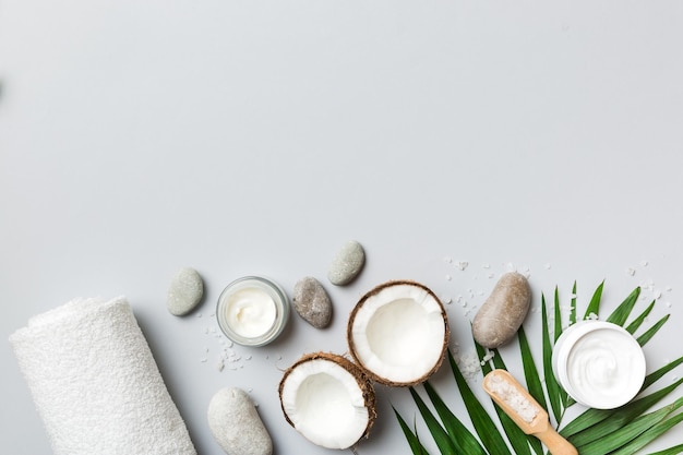 Kokosnuss mit Gläsern mit Kokosnussöl und kosmetischer Creme auf farbigem Hintergrund Ansicht von oben Freier Platz für Ihren Text Natürliche Spa-Kokoskosmetik und Bio-Behandlungskonzept Coconut Spa-Komposition