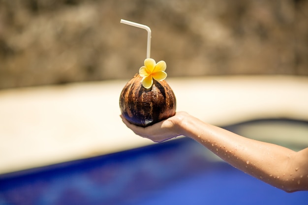 Kokosnussgetränk in der Frauenhand auf Schwimmbad.