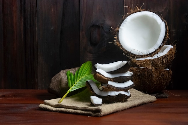 Kokosnusshälfte und Kokosnussstücke und -blatt auf Holztisch und schwarzem hölzernem Hintergrund