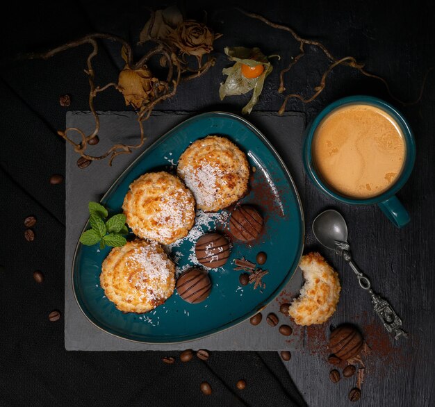 Kokosplätzchen mit Schokolade auf einem Teller mit einer Tasse Kaffee mit Milch auf schwarzem Hintergrund