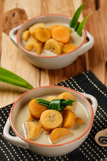 Kolak Pisang Ubi, compota de plátano y boniato, postre de sopa dulce indonesia a base de plátano, boniato, azúcar de palma y leche de coco. Plato popular durante el Ramadán. Sirve en Tazón Marrón.