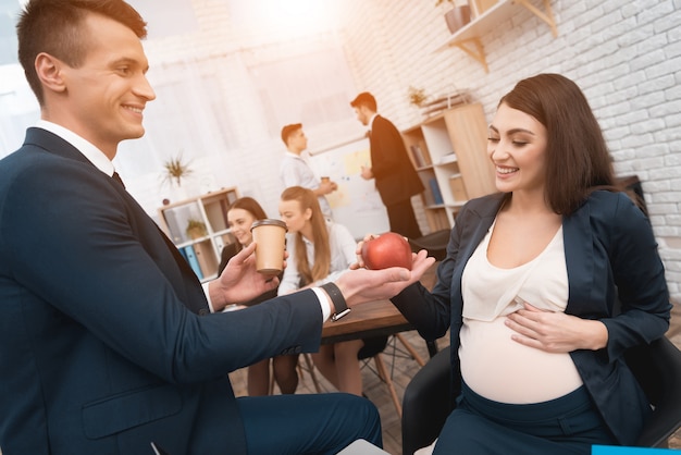 Kollege, der der schwangeren Arbeitskraft im Büro Lebensmittel gibt