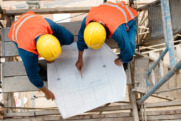 Foto kollegen mit sicherheitsausrüstung, die mit bauplänen arbeiten