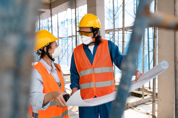 Foto kollegen mit sicherheitsausrüstung, die mit bauplänen arbeiten