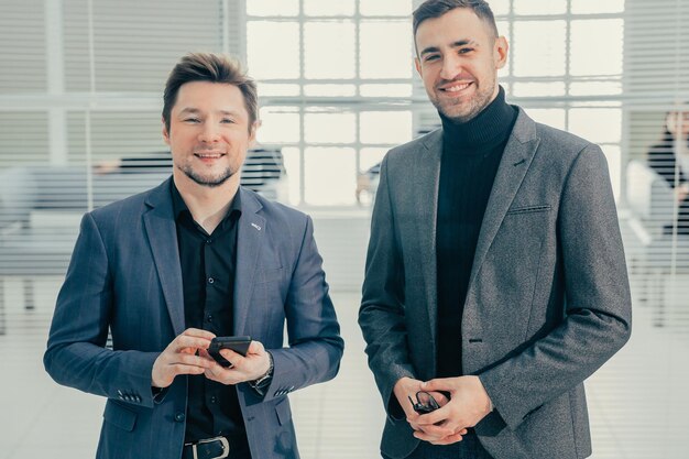 Kollegen mit Smartphone stehen in der Bürolobby. Foto mit einem Exemplarplatz.