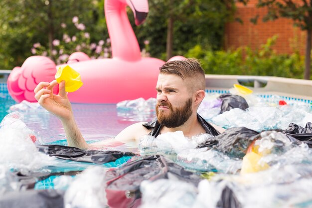 Ökologie, Plastikmüll, Umweltnotfall und Wasserverschmutzung - schockierter Mann schwimmt in einem schmutzigen Schwimmbad.