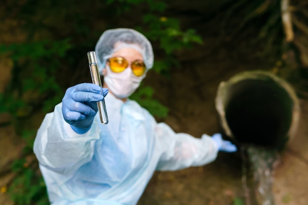 Ökologin oder Epidemiologin in Schutzkleidung und Maske zeigt ein Reagenzglas