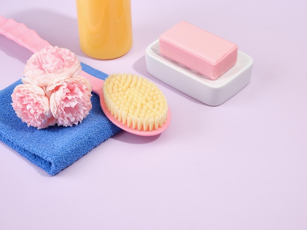 Ökologische Badeprodukte auf violettem Hintergrund Natürliche rosa Seife auf einer weißen Seifenschale, ein blau gewaschenes Duschtuch und eine rosa Bürste mit langem Griff für die Körperpflege Kopierraum für Text