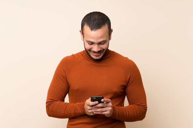 Kolumbianischer Mann mit dem Rollkragenpulli, der eine Mitteilung mit dem Mobile sendet