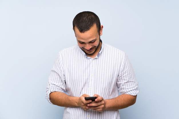 Kolumbianischer Mann über der lokalisierten blauen Wand, die eine Mitteilung mit dem Mobile sendet