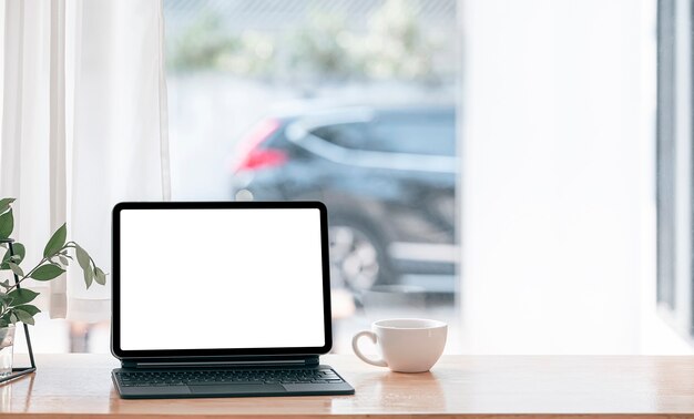 Komfortabler Arbeitsbereich zu Hause mit Tablett mit leerem Bildschirm und magischer Tastatur auf Holztisch.