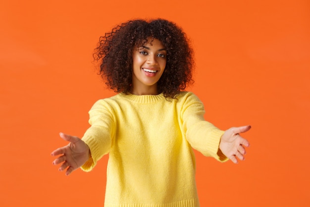 Komm her, lass mich dich umarmen. Nette freundliche, attraktive Afroamerikanerfrau mit lockigem Haar, Hände nach vorne streckend, bereit zum Kuscheln