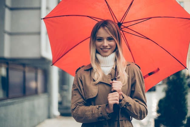 Komm zu mir unter meinen Regenschirm! Attraktive junge lächelnde Frau mit Regenschirm und Blick in die Kamera beim Stehen auf der Straße