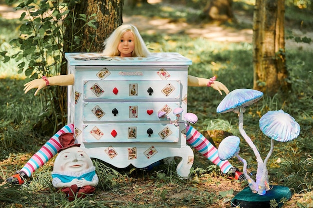 Kommode mit Puppe Alice drinnen in der Nähe von Humpty Dumpty und Kunstobjekt Pilze auf einer Kunstausstellung im Freien