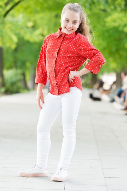 Kommt nie aus der Mode Entzückendes kleines Mädchen mit geflecktem Hemd im Street Fashion-Stil Kleines süßes Kind mit langer blonder Frisur am Sommertag Lässig ist ihr Stil