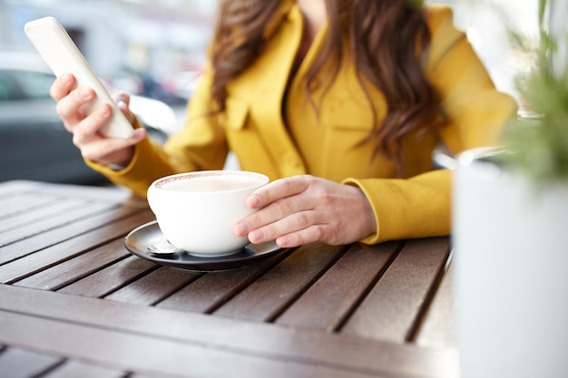 Kommunikations-, Technologie-, Freizeit- und Personenkonzept - Nahaufnahme einer jungen Frau oder eines Teenager-Mädchens, die auf dem Smartphone SMS schreibt und Kakao auf der Terrasse des Straßencafés der Stadt trinkt