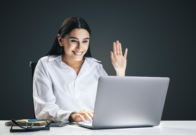 Kommunikationskonzept mit einer jungen hübschen Frau, die mit einem Kollegen über einen Online-Videodienst per Laptop chattet, isoliert auf dunkelgrauem Wandhintergrund, Nahaufnahme