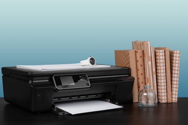 Kompakter Laserdrucker auf schwarzem Schreibtisch vor blauem Hintergrund
