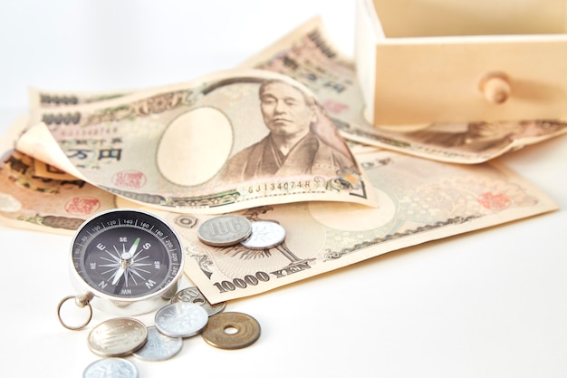 Kompass mit Banknoten der japanischen Yen und japanische Yen prägen auf weißem Hintergrund