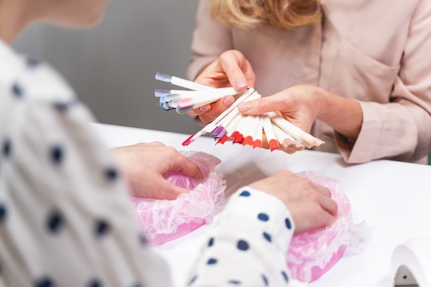 Kompetenter Meister, der ihrem Kunden gegenüber sitzt und die Farbpalette von Nagellack vorführt, Schönheitssalon