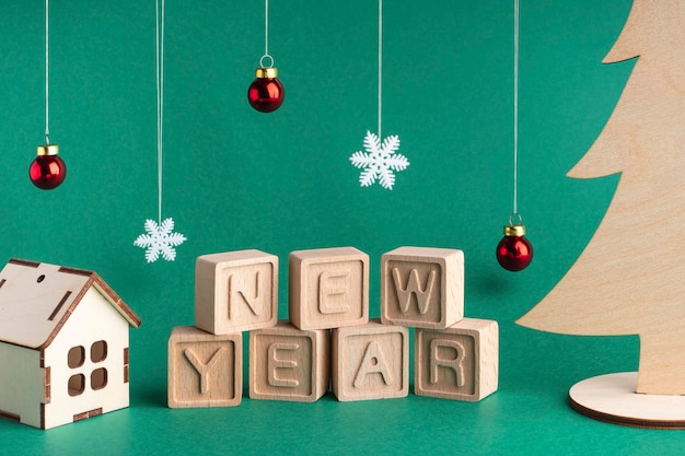 Komponiert das Wort Neujahr aus Holzwürfeln auf grünem Hintergrund Holzhaus Weihnachtsbaum und andere Weihnachtsschmuck Weihnachtskarte